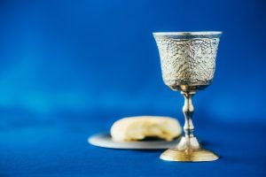 Communion still life. Unleavened bread, chalice of wine, silver kiddush wine cup on blue background